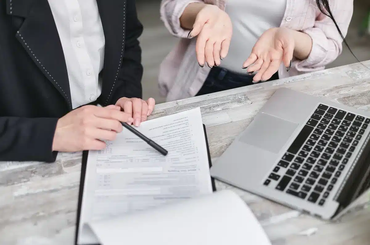 Close-up of hands holding a simple paper contract and a small house model on a wooden table; no logos, no faces